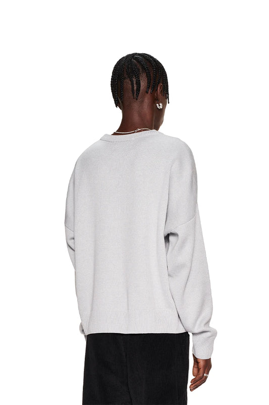 Frau trägt CC Knit Sweater Grau mit überschnittenen Schultern und OLAKALA Pin. Oversized Unisex-Passform, ideal für lässigen Stil.