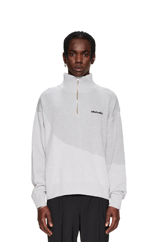 Ein Mann trägt einen weißen CC Knit Halfzip Pullover mit Reißverschluss, überschnittenen Schultern und versetztem Saum, kombiniert mit schwarzen Hosen.