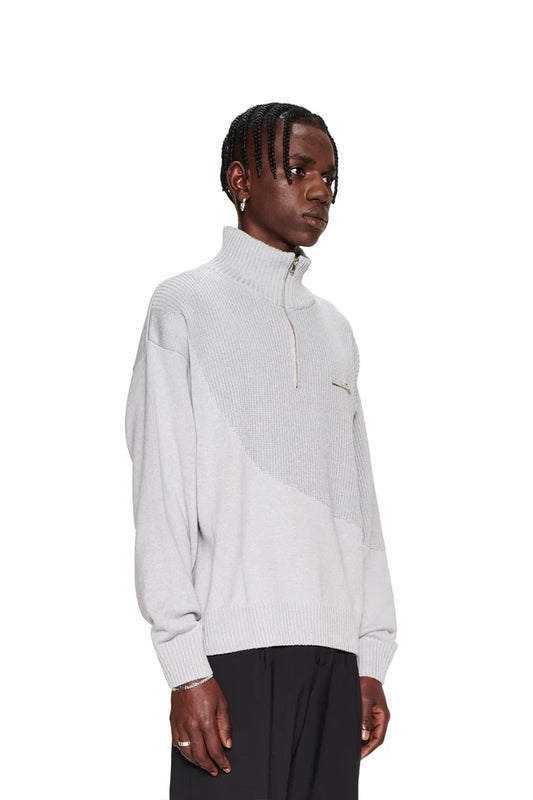Mann in weißem Strickpullover mit verschiedenen Mustern und überschnittenen Schultern, präsentiert OLAKALA's CC Knit Halfzip Gray in oversized Unisex-Passform.