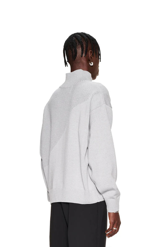 Frau trägt CC Knit Halfzip Gray, einen Strickpullover mit verschiedenen Mustern, überschnittenen Schultern und versetztem Saum. Oversized und unisex Design.