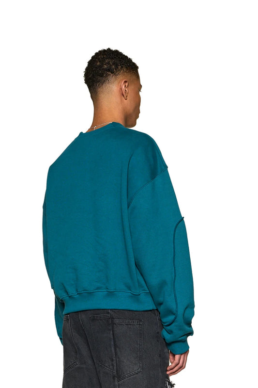 Mann trägt Defect ID Sweater Petrol mit Ripp-Bündchen und Digitaldruckgrafik auf der Brust, Oversized-Passform. Zeigt Rückansicht und Taschen-Detail.