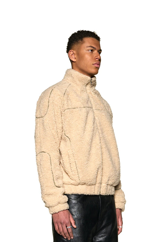 Mann in weißer Distorted Teddy Jacket mit Eingriffstaschen, gesticktem OLAKALA-Logo und elastischen Bündchen, zeigt Oversized-Passform und Unisex-Design.