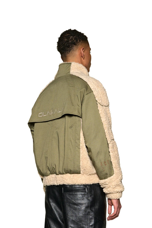 Mann trägt eine Distorted Teddy Jacket von OLAKALA mit gesticktem Logo auf der Brust und elastischen Bündchen, aus warmem Fleece und Rip-Stop-Gewebe.