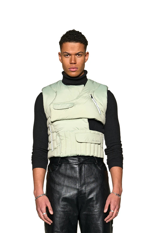 Man wears Anatomy Puffer Vest with asymmetrical cut and adjustable Velcro fastening. Two zipper and flap pockets, OLAKALA logo visible on the front.