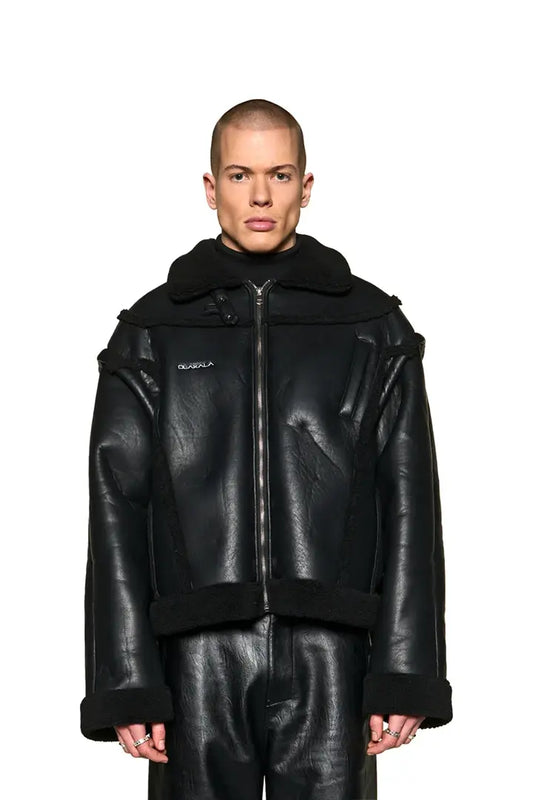 Mann trägt Anatomy Shearling Lederjacke mit abnehmbaren Ärmeln, Reißverschlusstasche, OLAKALA-Logo und veganem Lederimitat. Boxy Passform und Unisex-Design.