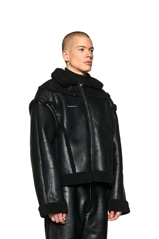 Anatomy Shearling Lederjacke mit abnehmbaren Ärmeln, Sherpa-Teilungsnähten und OLAKALA-Logo, getragen von einem Mann mit rasiertem Kopf.