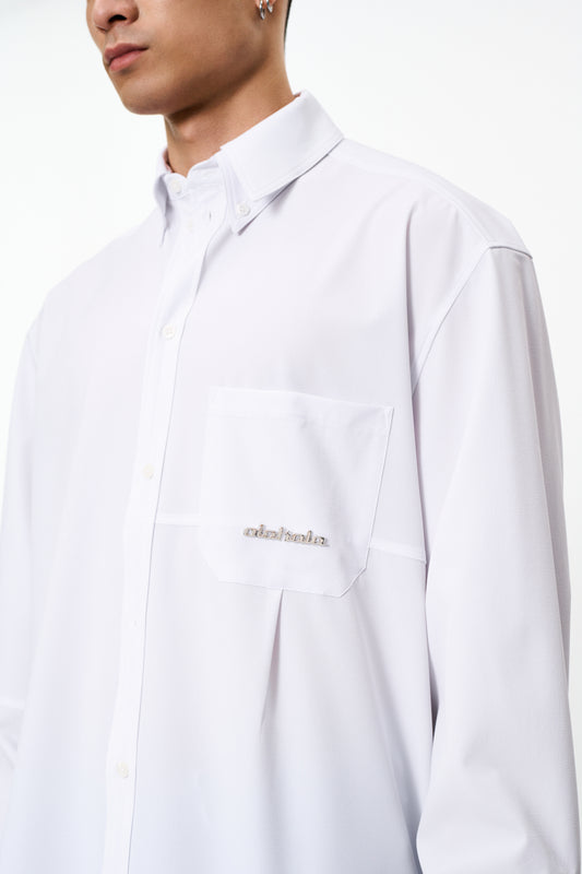 CC Button Shirt White: Nahaufnahme eines Hemdes mit doppeltem Kragen, Brusttasche mit Metall-Logo und Teilungsnähten, oversized Unisex-Passform von OLAKALA.