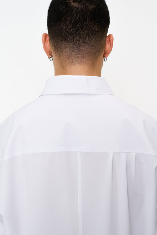 Rückansicht einer Person mit Ohrringen, die das CC Button Shirt White trägt, mit doppeltem Kragen und aufgesetzter Tasche mit OLAKALA Metall-Logo, oversized Unisex-Design.