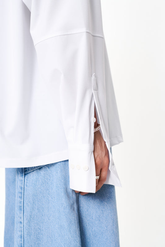 Person trägt das CC Button Shirt White mit doppeltem Kragen, Brusttasche mit Metall-Logo und Oversized-Passform. Unisex-Design, sichtbar sind Taschen- und Ärmel-Details.