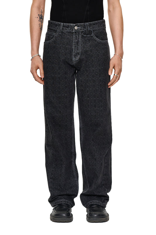Person trägt CC Black Monogram Denim Pants mit versetztem Hosenbund und „Mittelfinger“ Patch, lockere Passform, Geprägtes OLAKALA Patch sichtbar.