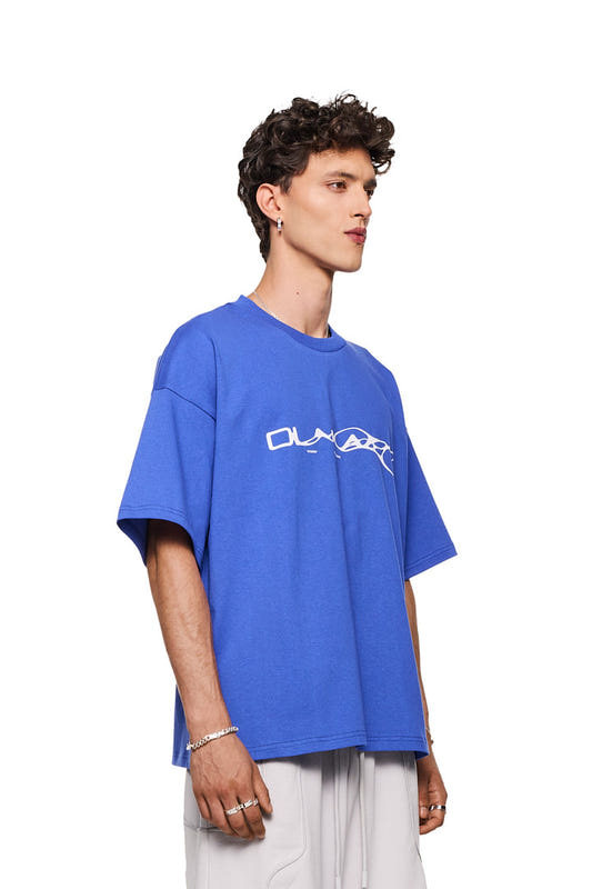 Mann trägt Synergy T-Shirt Blue mit weißem Siebdruck-Logo, oversized Fit. Der Unisex-Stil passt zum OLAKALA Onlineshop-Angebot.