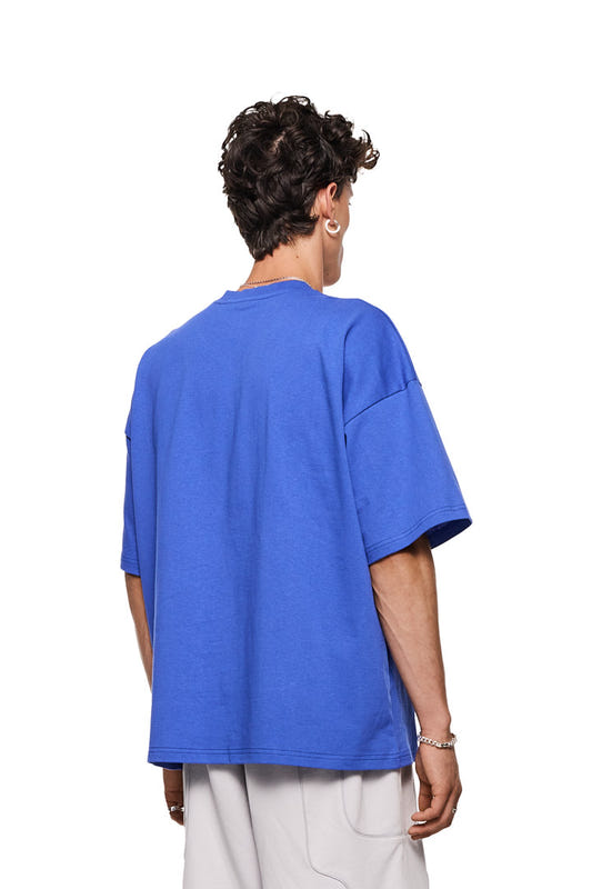 Synergy T-Shirt Blau, oversized, mit großem weißen Siebdruck-Logo auf der Brust, getragen von einer Person mit kurzem dunklem Haar, lässiger Look.