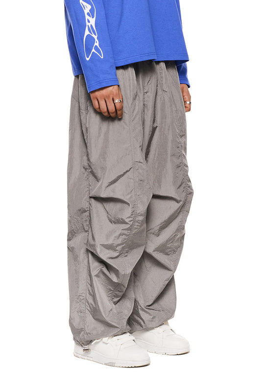 Person trägt Synergy Parachute Pants Gray mit Eingriffstaschen, elastischem Kordelzug und gesticktem Synergy-Logo, ideal für einen lässigen, unisex Look.