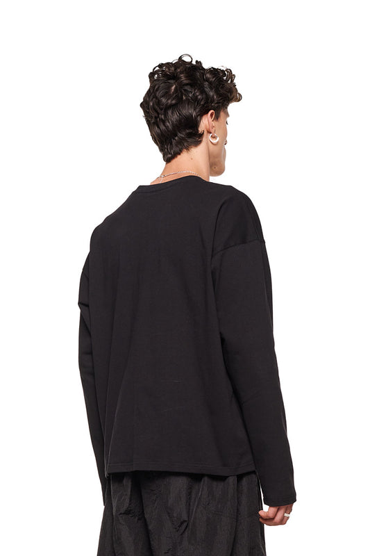 Person trägt Synergy Embroidered Longsleeve Black mit Ripp-Kragen und gesticktem Logo auf der Brust, oversized Passform, unisex Design von OLAKALA.