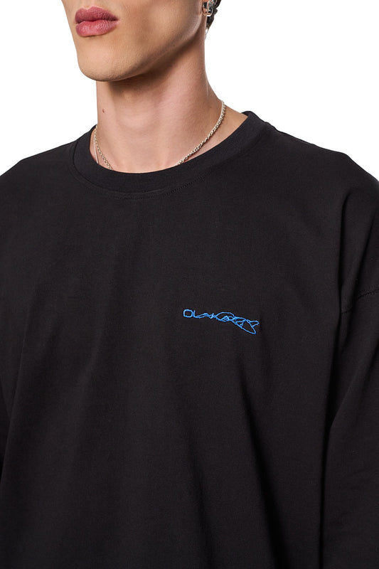 Person trägt ein schwarzes Synergy Embroidered Longsleeve mit Ripp-Kragen und gesticktem Logo auf der Brust, im oversized Unisex-Stil.