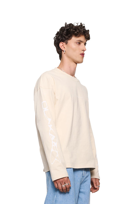 Mann im weißen Synergy Longsleeve Shirt Beige von OLAKALA, mit Siebdruck-Logo auf Brust und Ärmeln, oversized Unisex-Passform, zeigt Ring an der Hand.