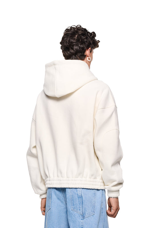 Person trägt Isolation Zip Hoodie Beige mit 2-Wege-Reißverschluss, Teilungsnähten, Eingriffstaschen und elastischen Bündchen. Oversized Passform und Isolation-Grafik auf der Brust.