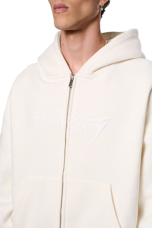 Person trägt einen Isolation Zip Hoodie Beige mit 2-Wege-Reißverschluss und Eingriffstaschen; Oversized-Passform; Teilungsnähte und elastische Bündchen sichtbar. Unisex-Design.