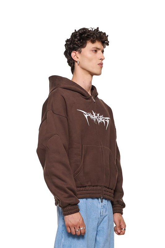 Isolation Zip Hoodie Brown mit 2-Wege-Reißverschluss, Teilungsnähten, Eingriffstaschen, elastischen Bündchen und Isolation-Grafik. Unisex, oversized Passform, getragen von einem Mann mit Ringen.