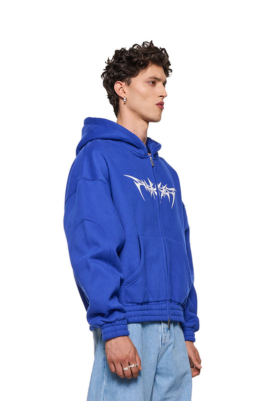Mann trägt Archive Isolation Zip-Hoodie Blau mit 2-Wege-Reißverschluss, Teilungsnähten, Eingriffstaschen, elastischen Bündchen, Isolation-Grafik und Oversized-Passform.
