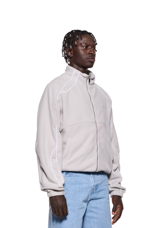 Mann mit Dreadlocks trägt eine graue Fleece Jacke Lunar Rock mit OLA KALA-Logo, Teilungsnähten und Eingriffstaschen, Oversized Fit, unisex.