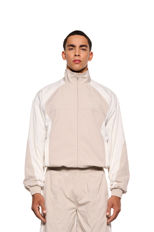 Mann in weiß-beigem Sports Tracksuit Jacket Sand mit gesticktem OLAKALA Sports Logo, elastischen Bündchen und Reißverschlusstaschen, zeigt lässige, unisex Passform.