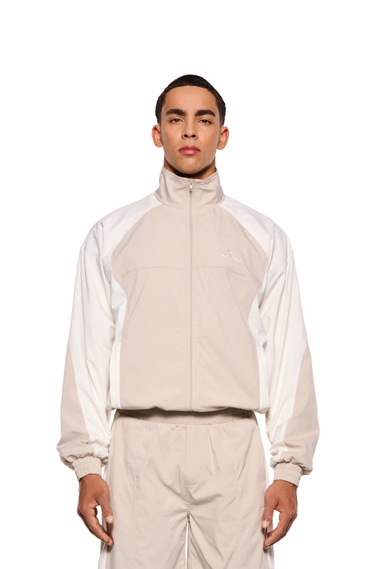 Mann in weiß-beigem Sports Tracksuit Jacket Sand mit gesticktem OLAKALA Sports Logo, elastischen Bündchen und Reißverschlusstaschen, zeigt lässige, unisex Passform.