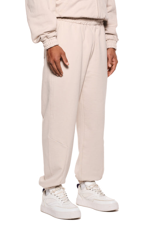 Person trägt Sports Sweatpants Beige von OLAKALA, zeigt weiße Sneakers, elastische Bündchen und Reißverschlusstaschen. Lockere Passform, unisex Jogginghose.
