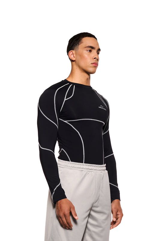 Mann im OLAKALA Sports Anatomy Tech Top Black mit Ziernähten und Logo auf der Brust, betont enganliegende Passform, unisex Design.