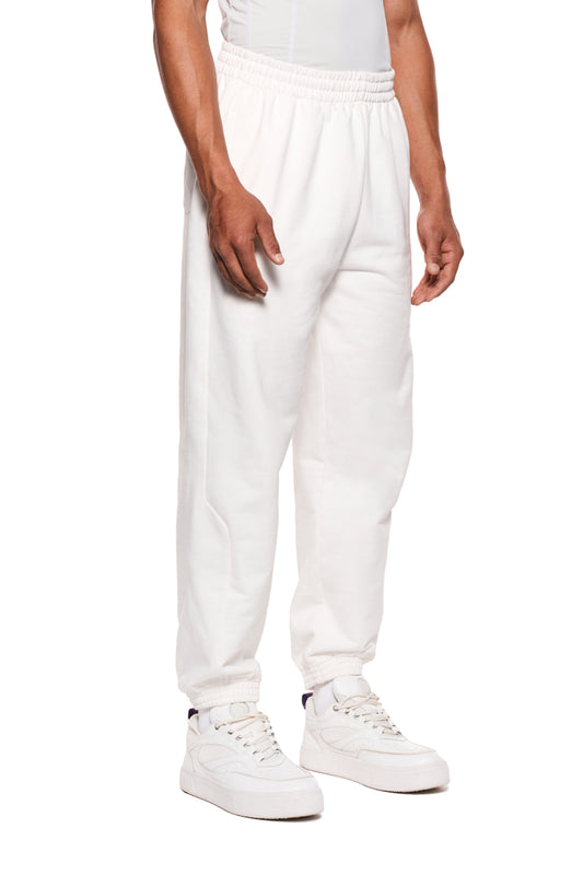Person trägt weiße Sports Sweatpants mit elastischem Bund, seitlichem Reißverschluss und gesticktem OLAKALA-Sport-Icon, kombiniert mit weißen Sneakern.