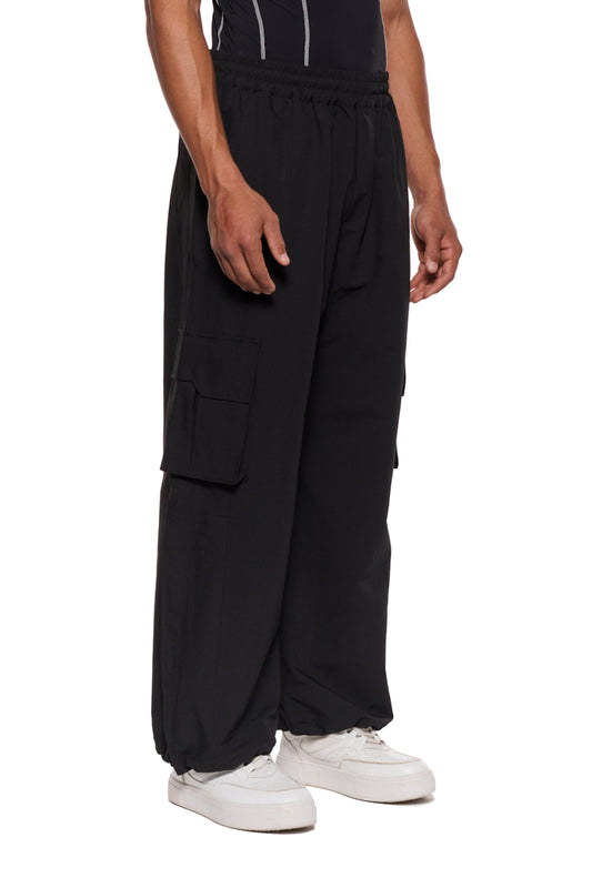 Mann trägt Synergy Cargo Pants Black mit elastischem Kordelzug und Cargotaschen mit Magnetverschluss, präsentiert im Offiziellen OLAKALA® Onlineshop.