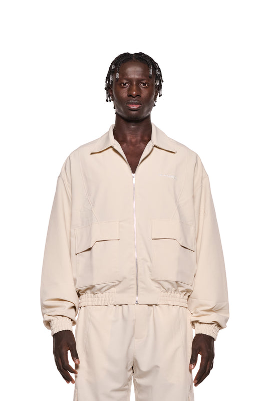 Mann in weißem Synergy Ripstop Jacket Sand mit Teilungsnähten, doppeltem Kragen und Cargo-Taschen, präsentiert von OLAKALA® Onlineshop.