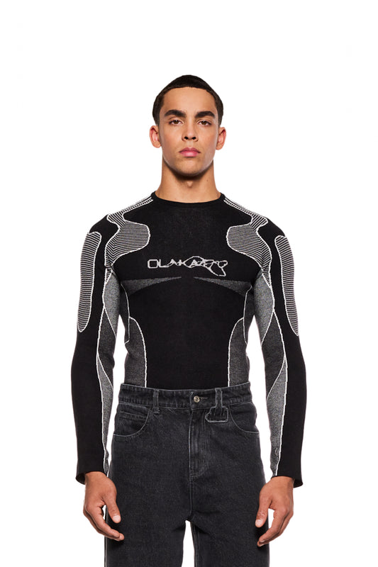 Mann trägt Synergy Anatomy Knit Tech-Top mit eingestricktem Synergy-Logo auf der Brust und Daumenschlaufen an den Ärmeln, eng anliegende Passform, unisex Design.