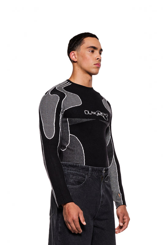 Mann trägt Synergy Anatomy Knit Tech-Top mit eingestricktem Synergy-Logo und Daumenschlaufen, betont eng anliegende Passform.