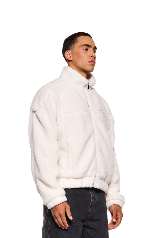Mann trägt Teddy Jacket Off White mit hohem Kragen, OLA KALA-Logo auf Brust, Reißverschlusstasche innen und Eingriffstasche vorne, oversized und cropped Fit.