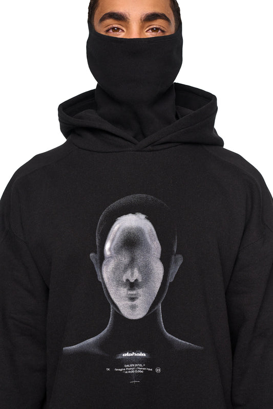 Person trägt das Alien Intel Mask Hoodie in Schwarz mit Kapuze und integrierter Maske, oversized und cropped Fit, mit Siebdruck-Grafik Alien Intel auf der Vorderseite.