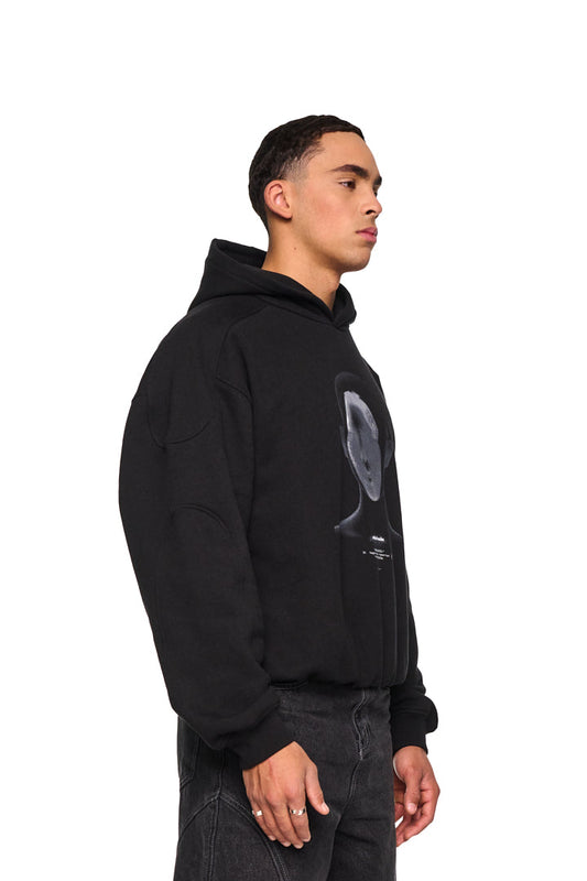 Mann in schwarzem Alien Intel Mask Hoodie, oversized und cropped, mit grauem Siebdruck und feinen Rippbündchen, präsentiert von OLAKALA.