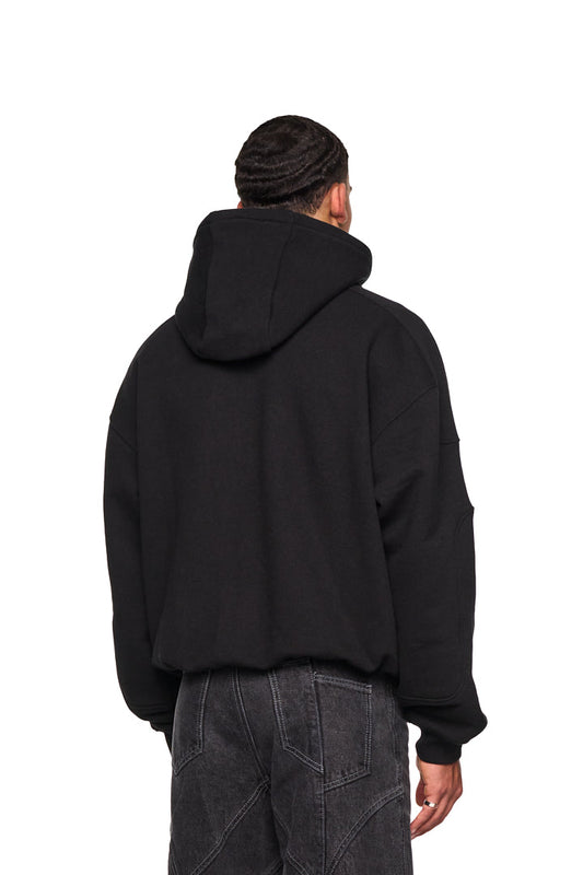Ein Mann trägt das Alien Intel Mask Hoodie mit Rippbündchen, elastischem Bund und grauem Alien Intel-Siebdruck, im oversized, cropped Fit. Unisex-Design.