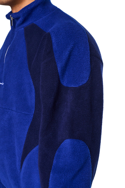 Nahaufnahme der Alien Intel Fleece Halfzip Blue Jacke mit hohem Kragen, Reißverschluss auf der Brust und gesticktem „Synergy“-Logo, aus weichem Fleece-Stoff und oversized Passform.
