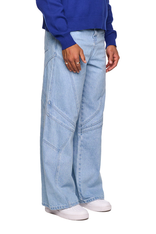 Person trägt Alien Intel Blue Denim Pants mit geradem Bein und lockerem Schnitt, im 5-Pocket-Style, sichtbare Teilungsnähte, geprägtes OLA KALA PU-Patch.