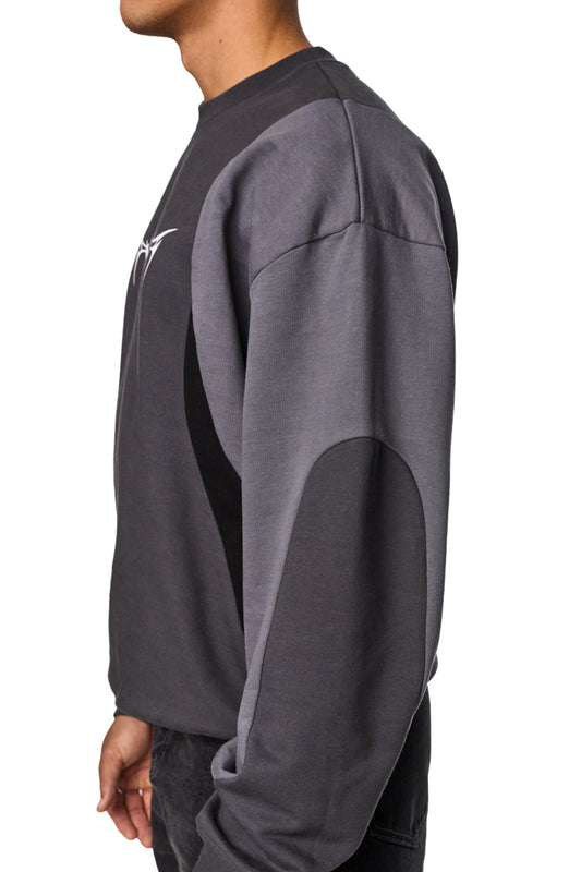 Person trägt Isolation Anatomy Sweater Grey mit großem, mittigem weißen Screenprint ISOLATION Thorn Font, leicht angerauter Innenseite und Stoffeinsätzen in verschiedenen Farbabstufungen.