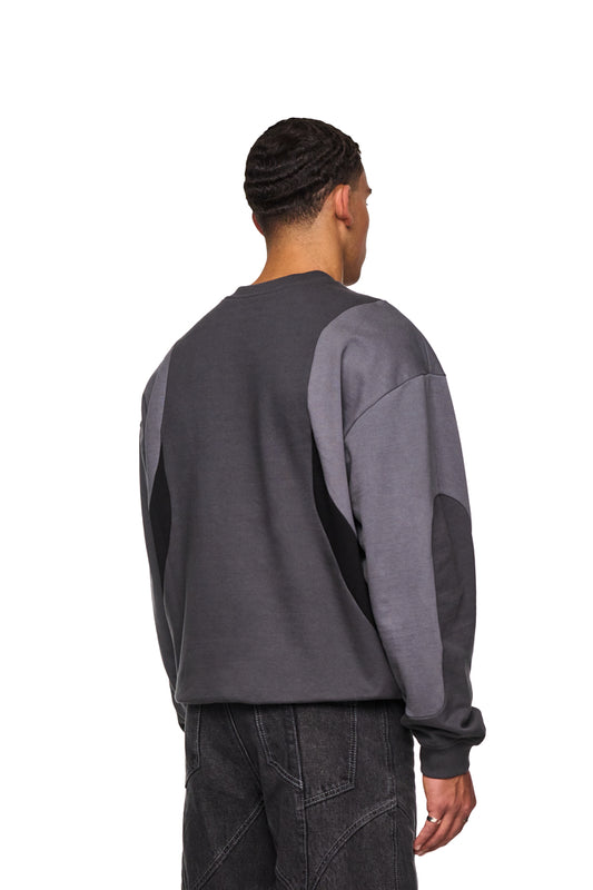 Mann im Isolation Anatomy Sweater Grey mit großem weißen Screenprint und Stoffeinsätzen, trägt graue Hose. Oversized Unisex Design von OLAKALA.