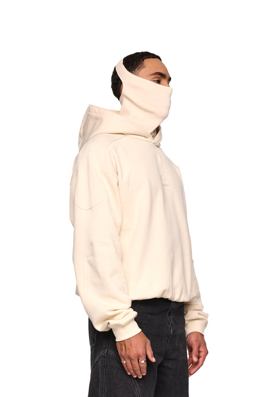 Ein Mann trägt den Discreet Mask Hoodie Beige mit integrierter Gesichtsbedeckung und gesticktem OLAKALA-Logo, oversized und cropped Fit.