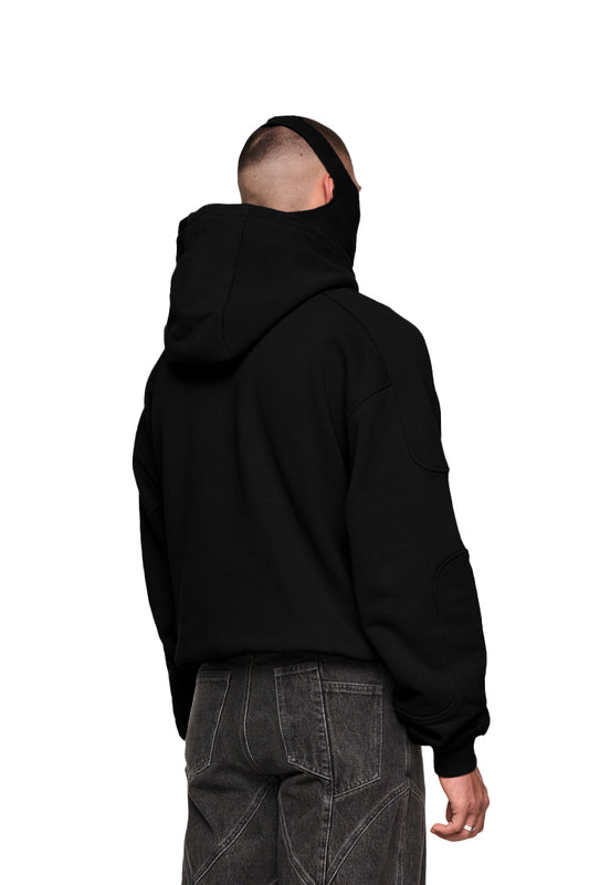 Mann trägt Discreet Mask Hoodie Black mit Ripp-Bündchen, elastischem Saum, gesticktem OLAKALA-Icon und integrierter Maske. Oversized und unisex Design.
