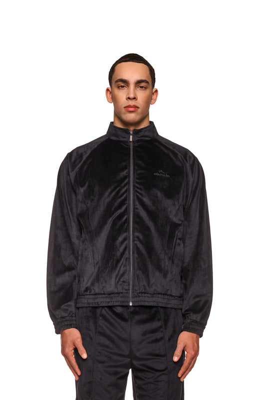 Ein Mann trägt die Sports Velour Jacket Black mit Reißverschluss, sportlichen Teilungsnähten und elastischen Bündchen, ideal für einen modernen, lockeren Look.