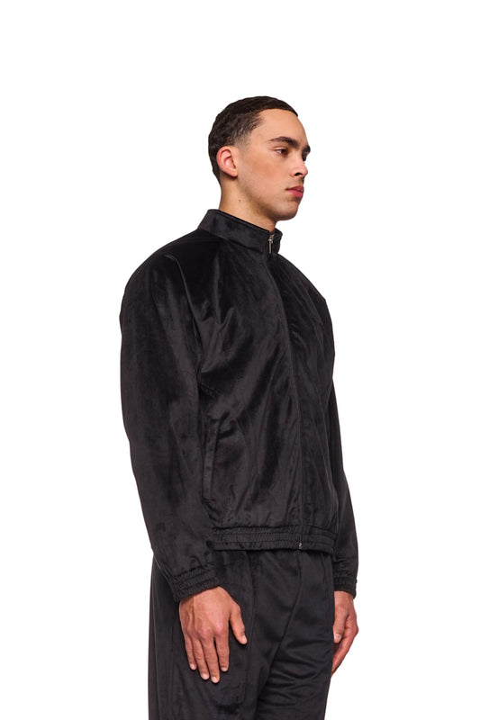 Mann trägt Sports Velour Jacket Black mit sportlich-modernen Teilungsnähten, weicher Velours-Haptik und elastischen Bündchen für bequeme Passform.