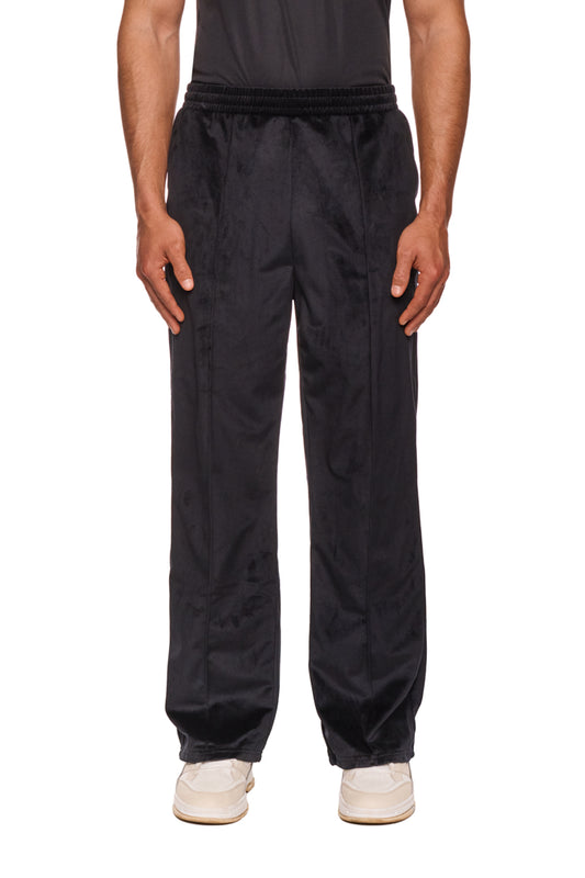 Ein Mann trägt die Sports Velour Jogger Pants Black mit offenem Beinabschluss, Eingriffstaschen und gesticktem OLAKALA Sports Icon auf dem linken Bein.