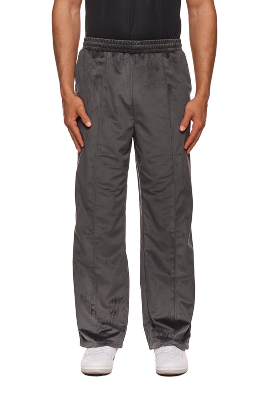 Person trägt Sports Velour Jogger Pants Gray, mit offener Beinabschluss, Eingriffstaschen, gesticktem OLAKALA-Sports-Icon und lockerer Passform.