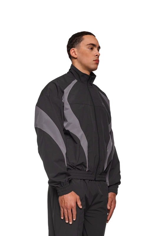 Mann in schwarzer Sports Trackjacket aus strapazierfähigem Rip-Stop-Gewebe mit gesticktem OLAKALA Sports Logo, elastischem Bund und Ärmeln für optimalen Tragekomfort.