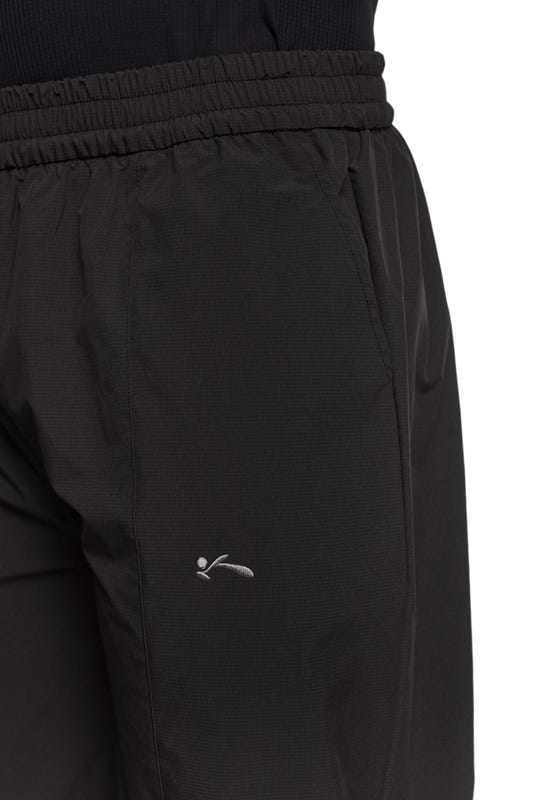 Nahaufnahme von OLAKALA Sports Trackpants in Schwarz mit sportlichen Kontrasteinsätzen, elastischem Bund und gesticktem Logo auf dem linken Bein.